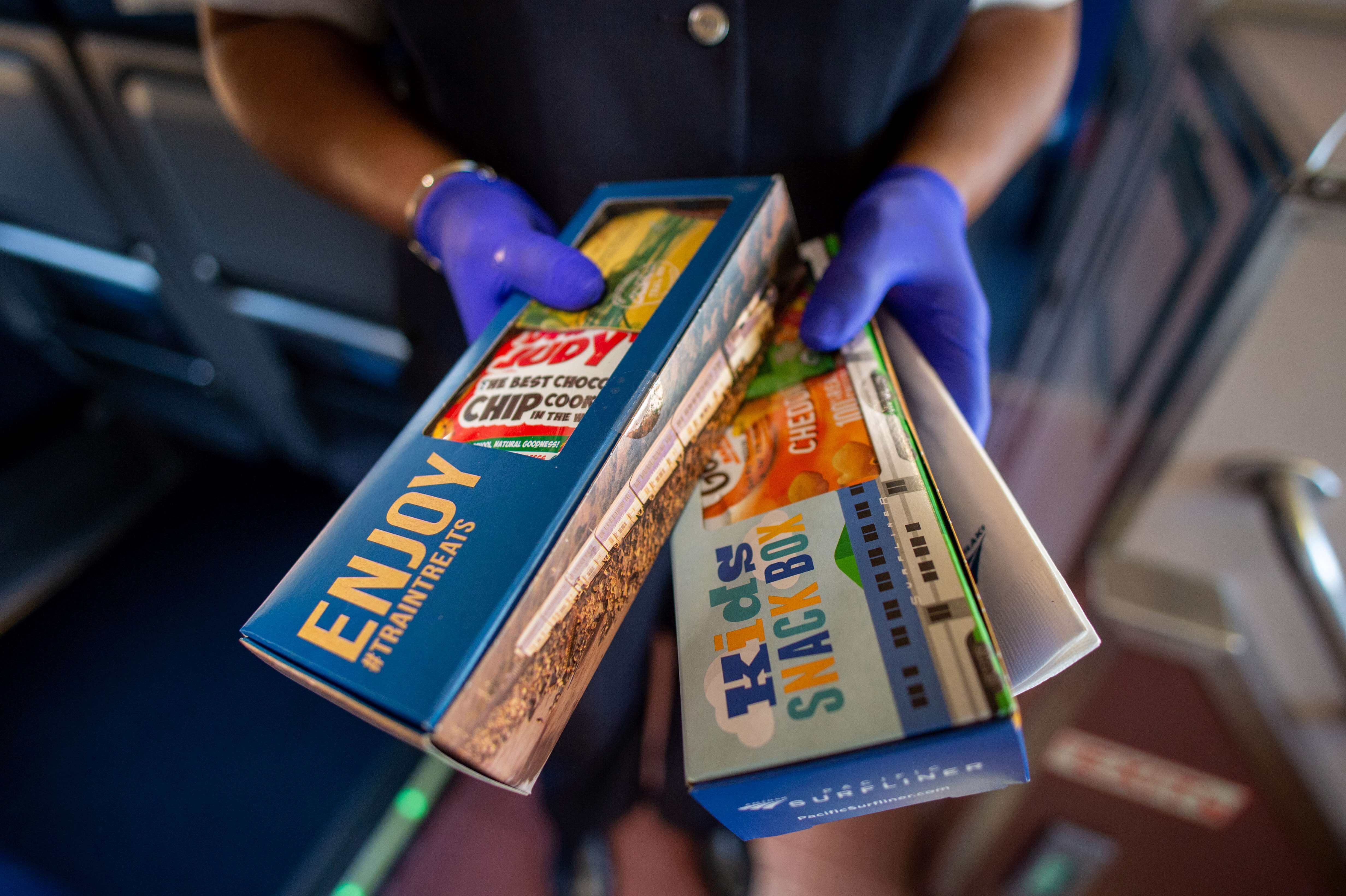An attendant onboard the Amtrak Pacific Surfliner offers Business Class and kids snack boxes to the camera.