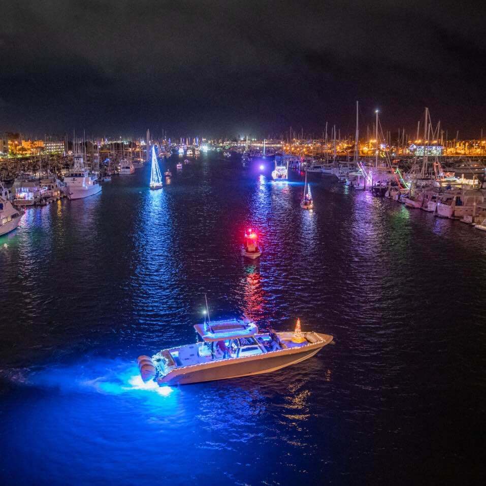 Channel Islands Harbor at night. Boats adorned with bright Christmas lights are docked on either side of the water.