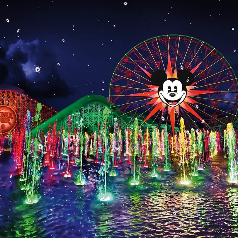 A nighttime holiday show in front of California Adventure’s Pixar Pier, with colorful fountains of water and bright lights.