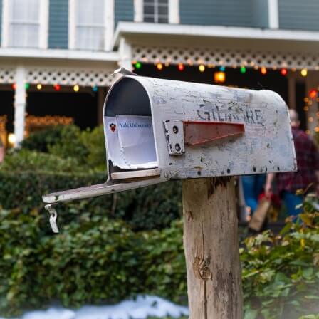 An open mailbox with the name “Gilmore” in faded letters on the side. A letter addressed from Yale University peaks out.