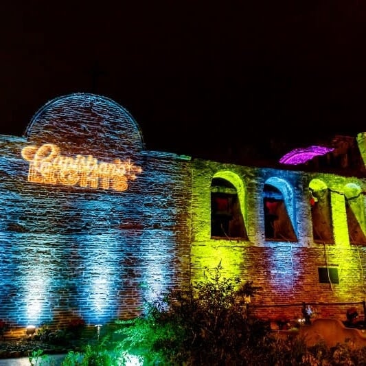 Mission San Juan Capistrano illuminated at the annual Capistrano Lights event with warm golden lights and tall palm trees.