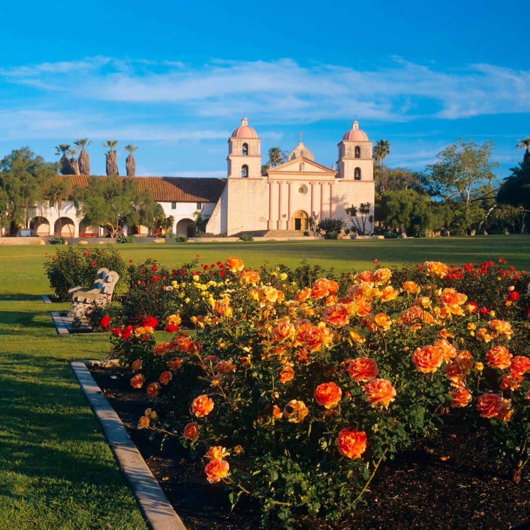 A shot of the rose garden in front of the Santa Barbara Mission, with orange, red, and yellow flowers.